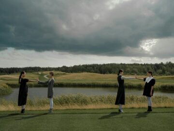 Four women maintaining social distance in a dramatic, cloudy outdoor setting.
