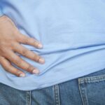 A person in a blue shirt and jeans clutching their hip, possibly indicating pain.