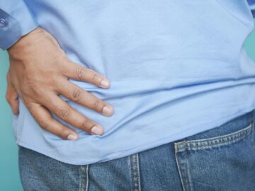 A person in a blue shirt and jeans clutching their hip, possibly indicating pain.