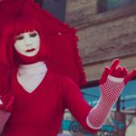 A striking image of a street performer in a red costume with an umbrella, showcasing unique fashion and makeup.