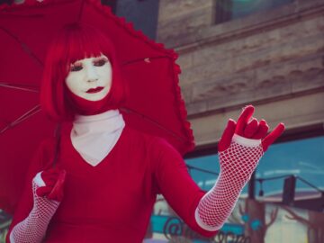 A striking image of a street performer in a red costume with an umbrella, showcasing unique fashion and makeup.