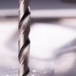 Detailed close-up of a steel drill bit cutting through metal surface, showcasing metalworking precision.