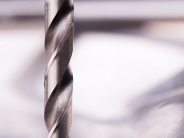 Detailed close-up of a steel drill bit cutting through metal surface, showcasing metalworking precision.