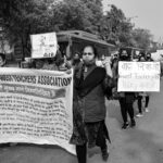 A group of individuals protest for teachers' rights, holding signs and banners on a city street.