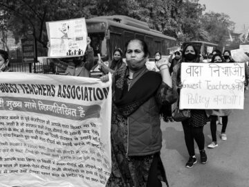 A group of individuals protest for teachers' rights, holding signs and banners on a city street.