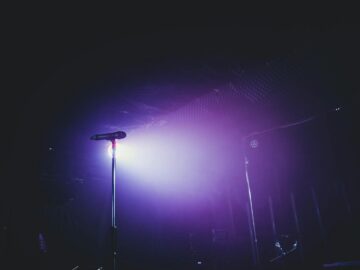 A moody stage setup with a microphone under purple lighting, perfect for concerts.