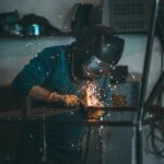 Skilled welder works with sparks in an industrial workshop setting, wearing safety gear.