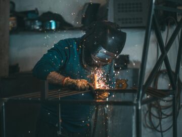Skilled welder works with sparks in an industrial workshop setting, wearing safety gear.