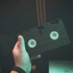 A hand holds a classic VHS tape, capturing a nostalgic moment in a dimly lit room.