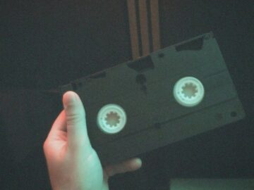A hand holds a classic VHS tape, capturing a nostalgic moment in a dimly lit room.