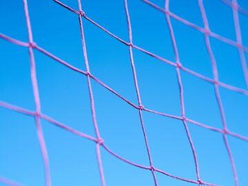 Close-up of a pink volleyball net pattern against a clear blue sky, showcasing geometric shapes.