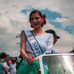 A pageant contestant smiles while sitting on a car in Mérida, showcasing vibrant urban culture.