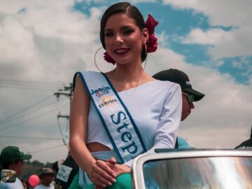 A pageant contestant smiles while sitting on a car in Mérida, showcasing vibrant urban culture.