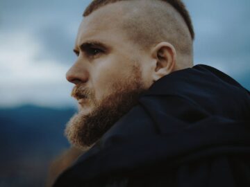Portrait of a bearded man with mohawk hairstyle, gazing intensely outdoors.