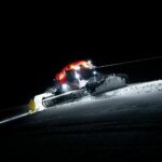 Snow groomer smoothing ski slopes in Zermatt, Switzerland at night.