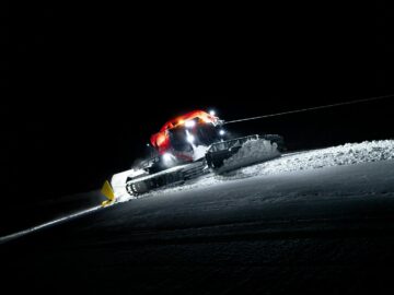 Snow groomer smoothing ski slopes in Zermatt, Switzerland at night.