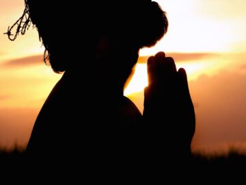 A silhouette of a man praying at sunset, wearing a crown of thorns, symbolizing faith and hope.