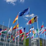 Low angle view of European Union flags on flagpoles against a blue sky, symbolizing unity.