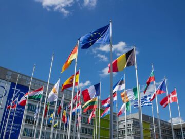 Low angle view of European Union flags on flagpoles against a blue sky, symbolizing unity.