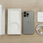 Flat lay view of the newest Apple iPhone model, box, and charging accessories on a wooden table.