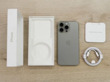 Flat lay view of the newest Apple iPhone model, box, and charging accessories on a wooden table.