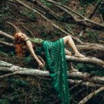 A woman in a green dress gracefully reclines on forest branches, creating a serene and mystical atmosphere.