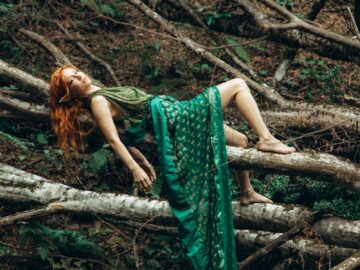 A woman in a green dress gracefully reclines on forest branches, creating a serene and mystical atmosphere.