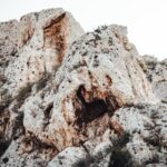 A rugged rocky cliff face featuring natural caves and scattered vegetation, showcasing the raw beauty of nature.