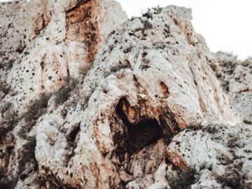 A rugged rocky cliff face featuring natural caves and scattered vegetation, showcasing the raw beauty of nature.