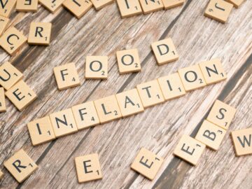 Wooden scrabble tiles arrange to spell 'Food Inflation' on a rustic wooden surface, conceptually depicting rising food prices.