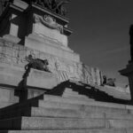Low angle shot of a grand stone monument with sculptures and stairs, under daylight.