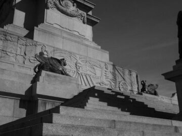 Low angle shot of a grand stone monument with sculptures and stairs, under daylight.