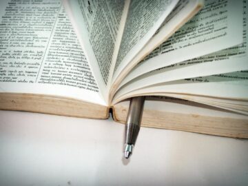 A close-up of an open dictionary with a pen separating the pages for convenient reference.