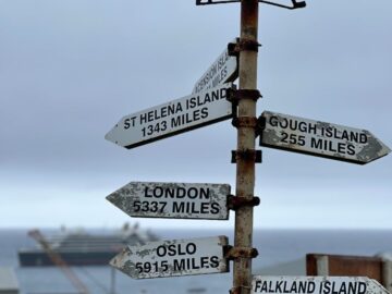 Signpost on Tristan da Cunha indicating distances to various locations, with ocean backdrop.