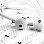 Close-up of white earphones resting on sheet music, emphasizing music and sound themes.