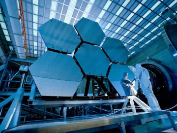 Engineers in protective suits work on telescopic mirrors in a high-tech lab.
