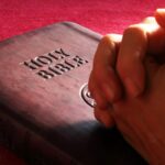 Close-up of hands praying on a Holy Bible, symbolizing faith and spirituality.