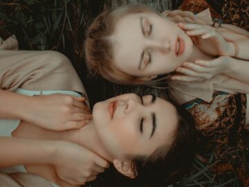 Two women relaxing outdoors, eyes closed, enjoying a peaceful moment in nature.