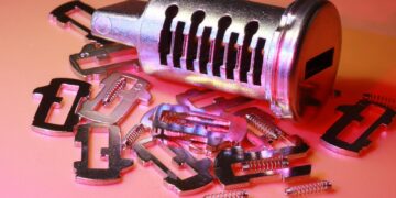 Detailed image of a disassembled lock cylinder and its metal components on a colored surface.