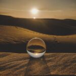 A captivating scene of a crystal sphere reflecting the vast desert landscape at sunset, creating a serene atmosphere.