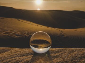 A captivating scene of a crystal sphere reflecting the vast desert landscape at sunset, creating a serene atmosphere.
