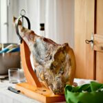 A beautifully displayed cured ham on a wooden stand in a bright kitchen setting, perfect for gourmet dining.