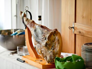 A beautifully displayed cured ham on a wooden stand in a bright kitchen setting, perfect for gourmet dining.