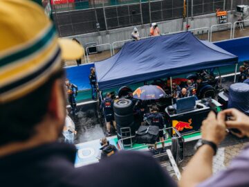 A bustling Formula One pit stop viewed from above with spectators in the foreground.