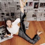 Woman posing creatively on floor in studio with newspaper backdrop.