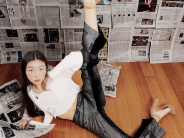 Woman posing creatively on floor in studio with newspaper backdrop.