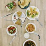 Top view of assorted Asian dishes with utensils and snacks on a wooden floor.