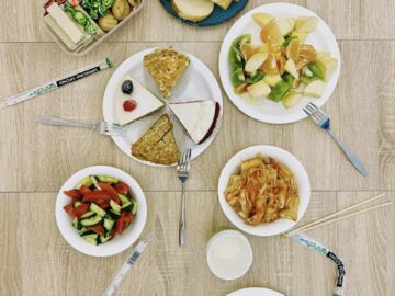Top view of assorted Asian dishes with utensils and snacks on a wooden floor.