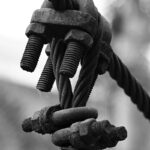 Black and white close-up of a cable tension system with bolts and rust detailing.