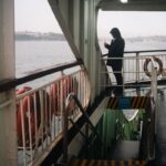 Silhouette of a person on a ferry using a phone with water view.
